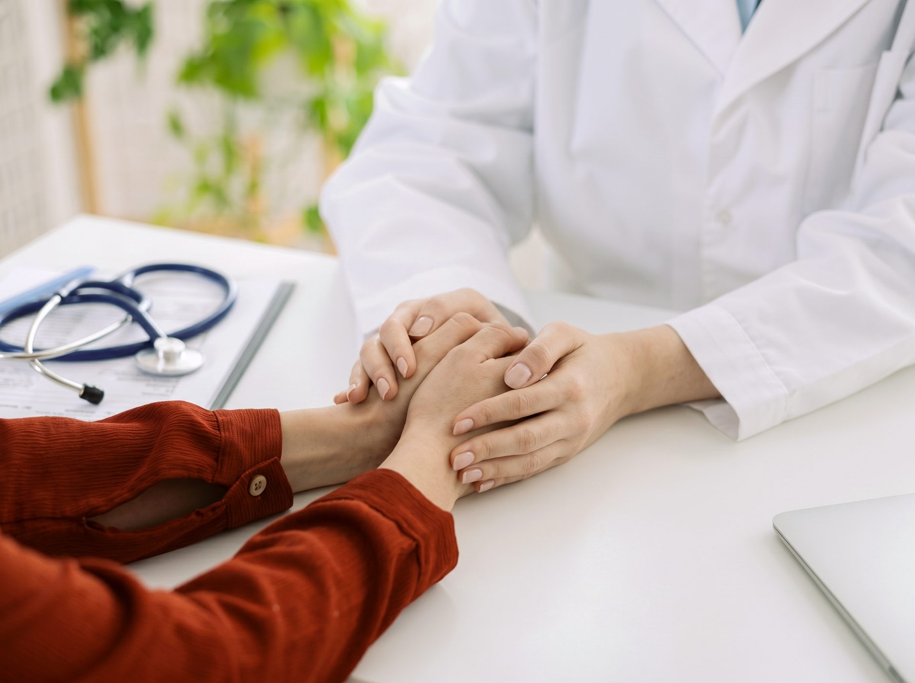 A caregiver holding a patient's hands beside a stethoscope