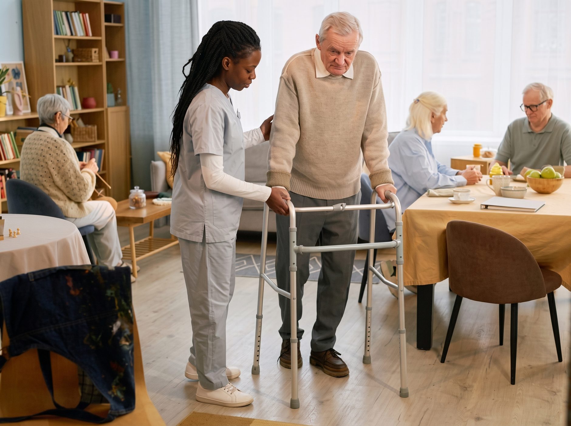 Caregiver helping a resident walk through a care home dining room